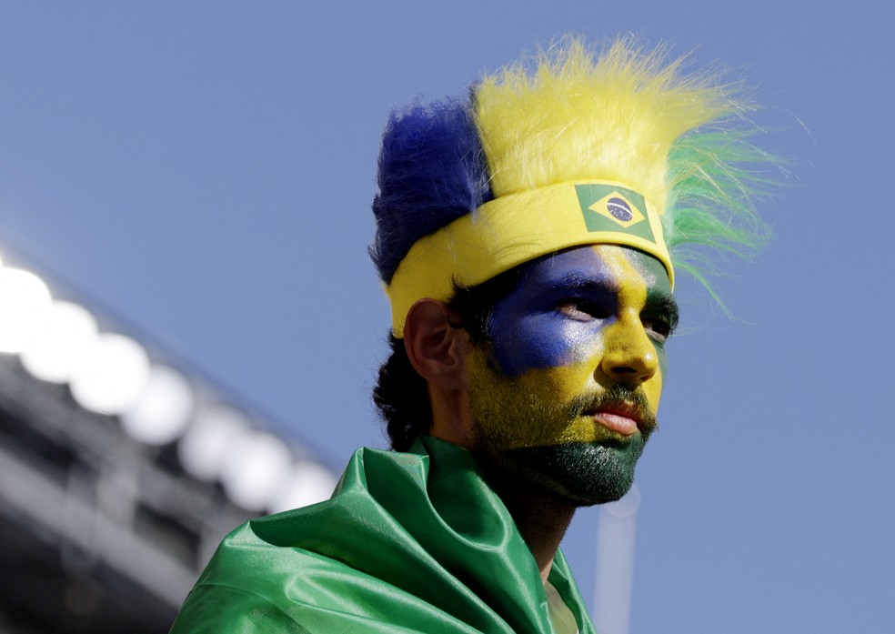 Torcedor com rosto pintado e tira com fiapos nas cores da bandeira brasileira