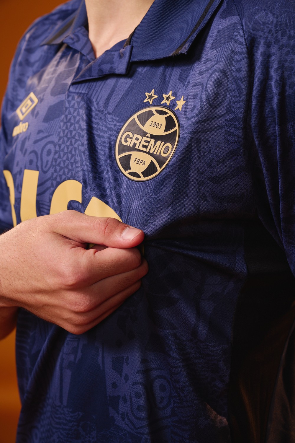 Detalhe do escudo em dourado e dos grafismos sutis no tecido