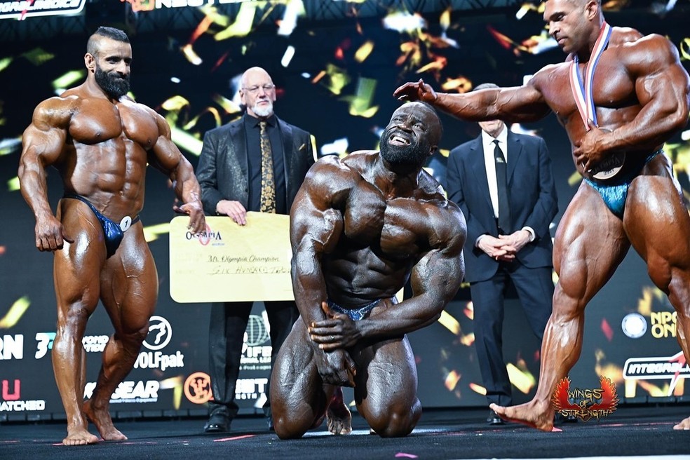 Samson Dauda desaba ao ser anunciado o Mr. Olympia de 2024 e é acudido por Hadi Choopan (esq.) e Derek Lunsford, os campeões anteriores — Foto: Reprodução/Instagram