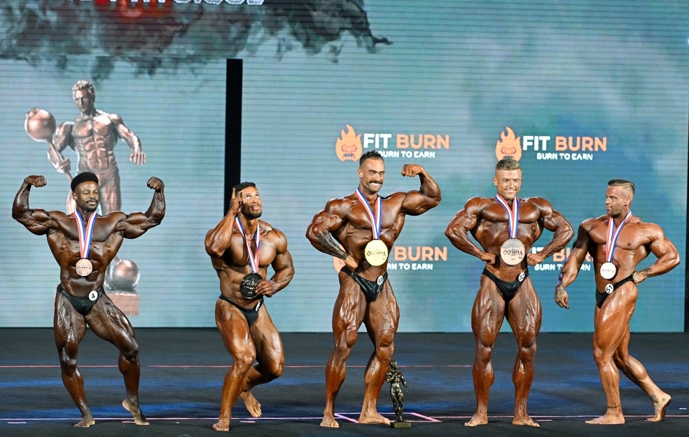 Chris Bumstead no centro do palco com a medalha de campeão. À sua esquerda, o brasileiro Ramon Dino. — Foto: Diamond Images/Getty Images