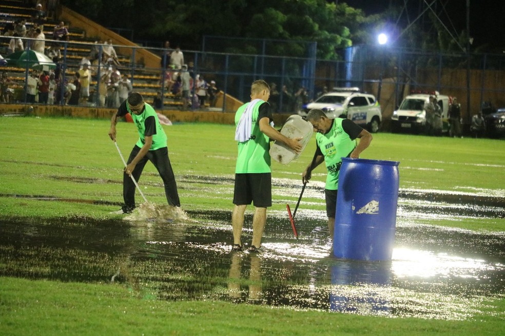 Funcionários usam rodo para tirar excesso de água do gramado do Estádio Lindolfo Monteiro — Foto: Julio Costa