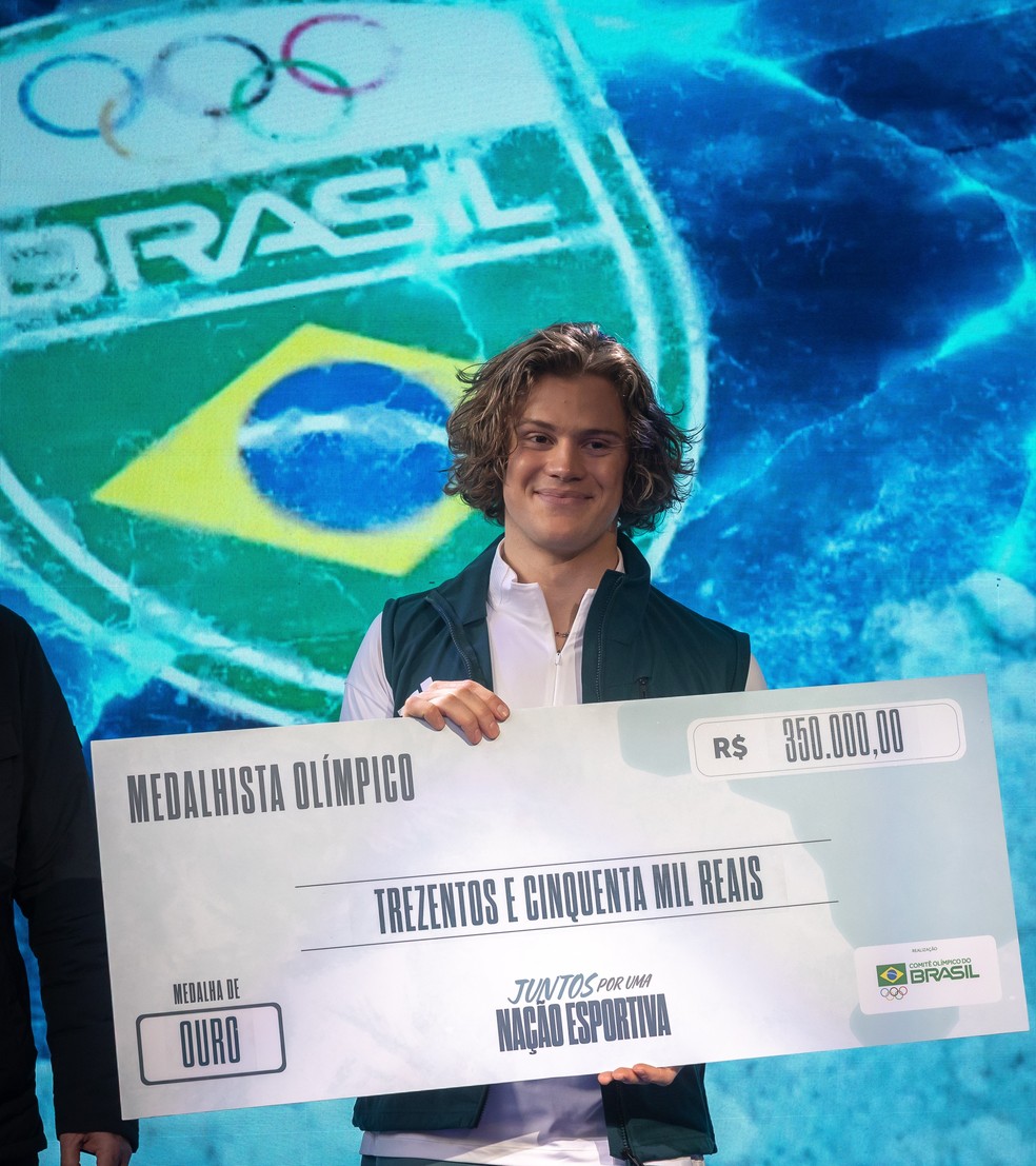 Lucas Pinheiro posa com "cheque" de premiação do COB por ouro olímpico — Foto: Jonne Roriz/COB