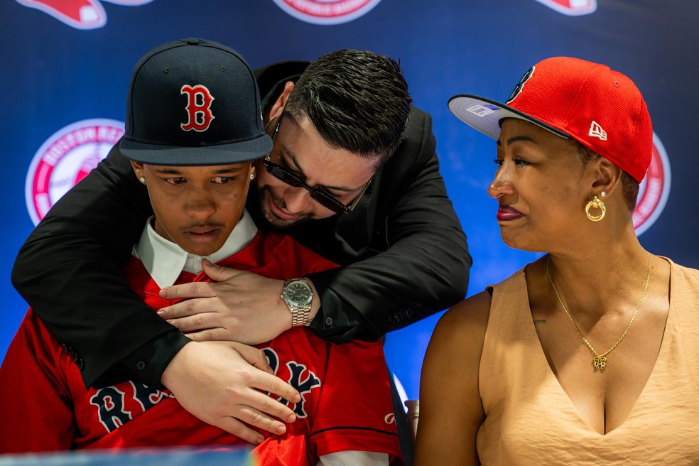 Ao lado da mãe, Cláudio Pereira se emociona ao assinar com o Boston Red Sox e é consolado pelo empresário, Giovanny Cordero — Foto: Divulgação/Red Sox