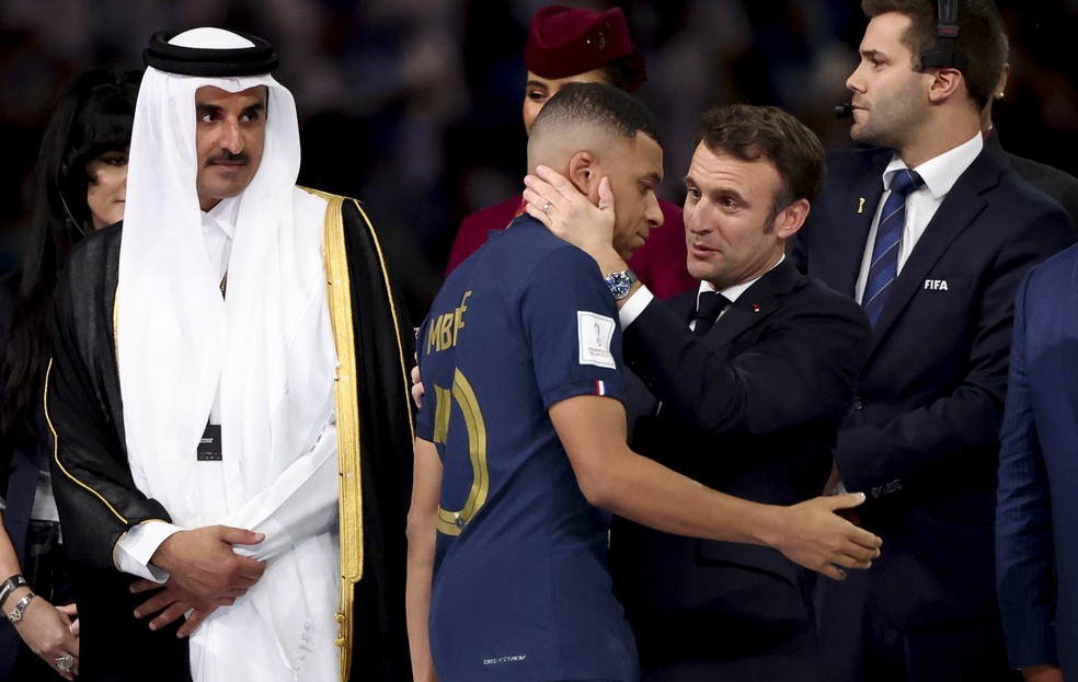 Mbappé é consolado pelo presidente da França, Emmanuel Macron, e observado pelo emir do Catar, Tamim bin Hamad al-Thani, na final da Copa do Mundo de 2022 — Foto: Jean Catuffe/Getty Images