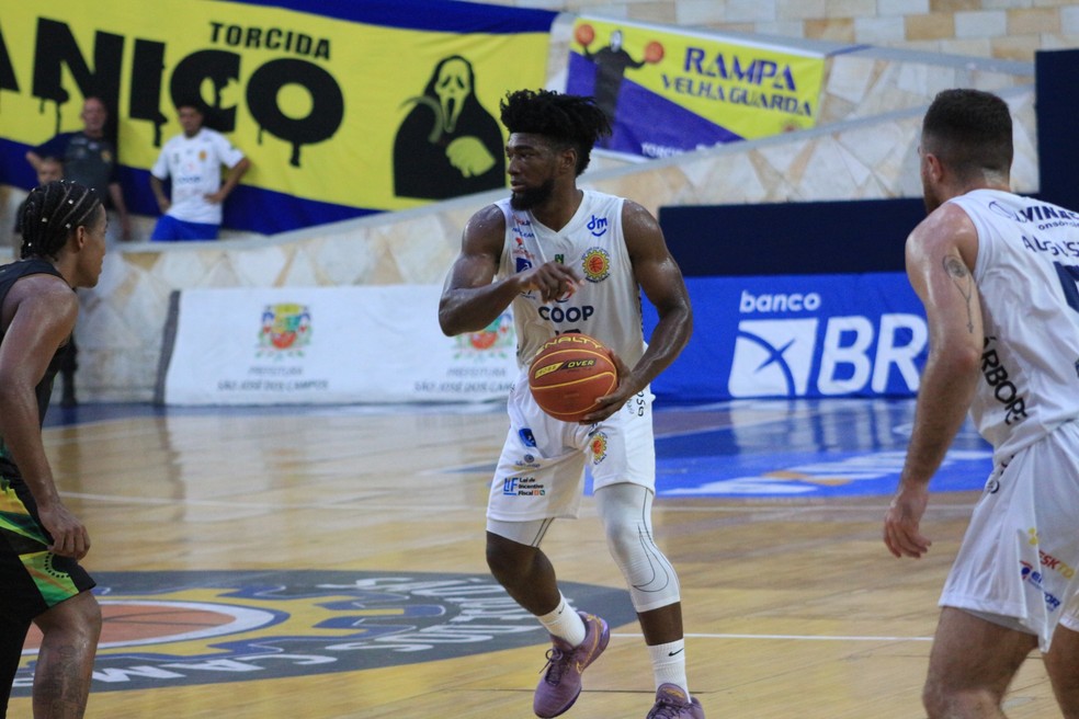 Jogador do São José Basquete conduz a bola durante partida, enquanto é marcado por adversário. O duelo acontece em ginásio com torcida ao fundo.