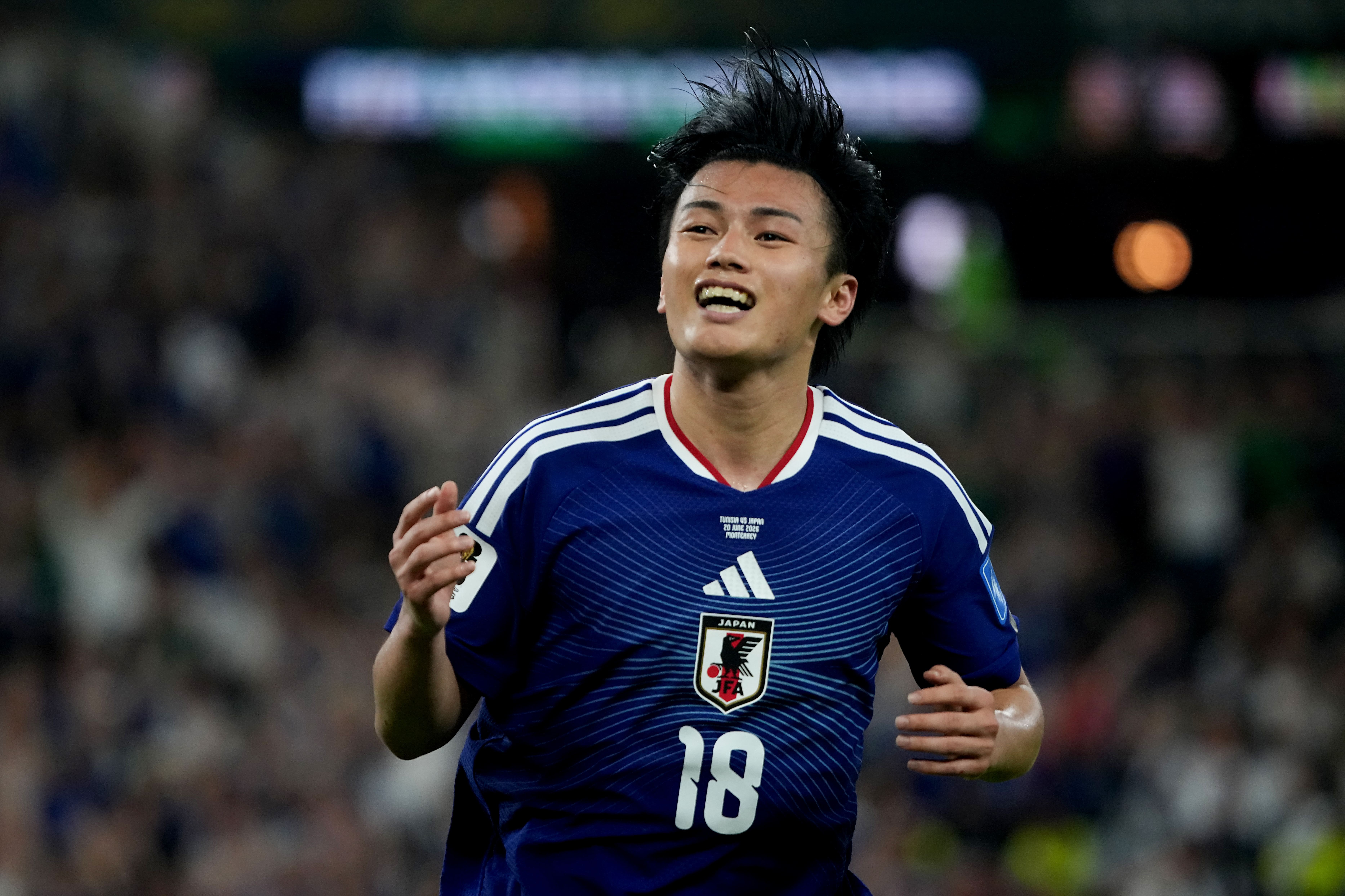 Ayase Ueda em ação durante partida oficial, vestindo o uniforme da seleção japonesa com expressão focada no jogo.