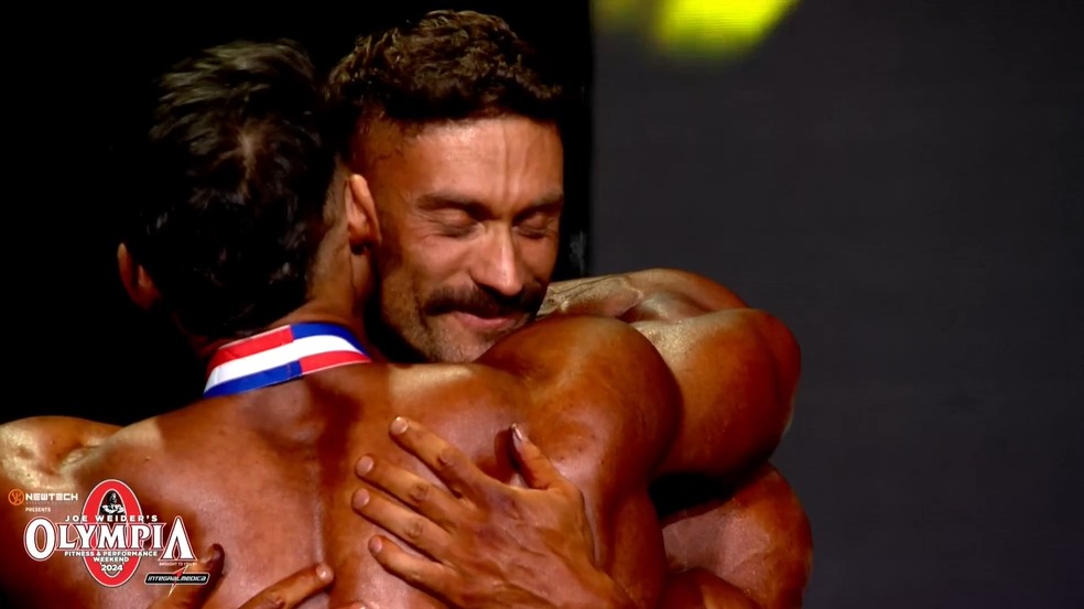 CBum é abraçado por Ramon Dino ao ser anunciado campeão da Classic Physique no Mr. Olympia 2024 — Foto: Reprodução/Olympia TV